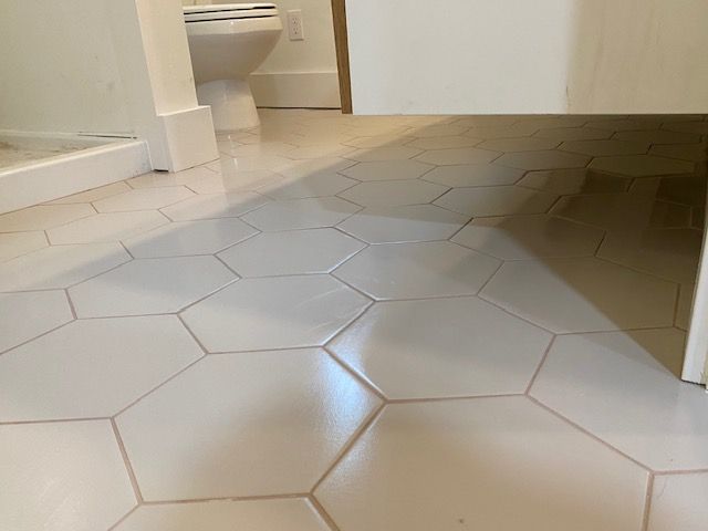 White hexagonal bathroom floor tiles with a dark shadow across the room and a toilet in the background