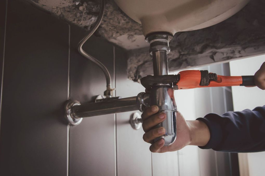 Plumber tightening a bathroom sink drain with pliers under a white basin