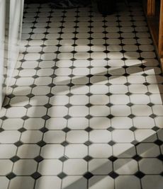 A person wearing pink gloves is cleaning a tiled floor with a brush.