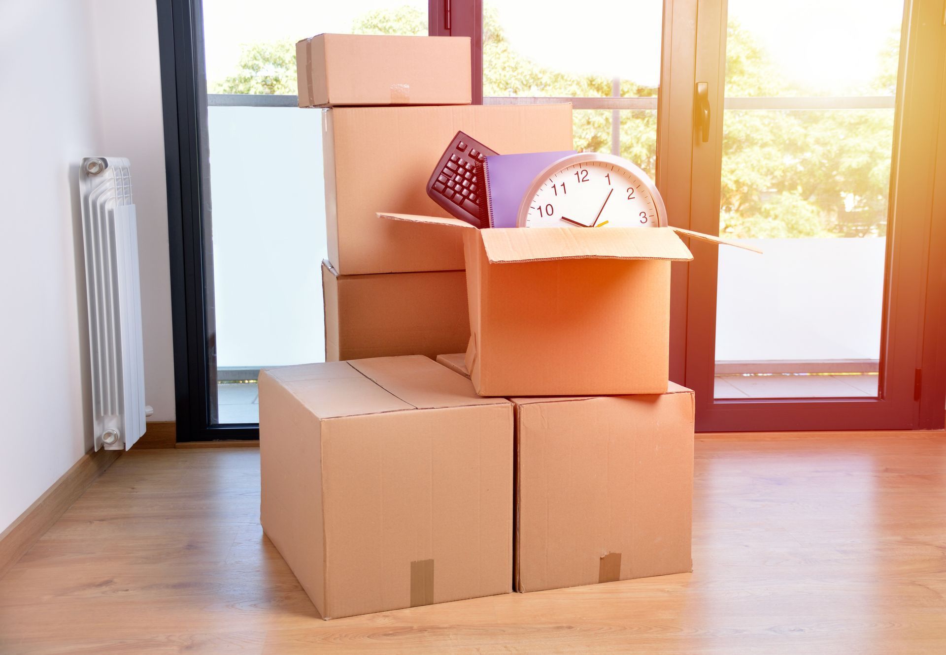 Cardboard boxes stacked in a room with a window, containing household items, ready for moving.