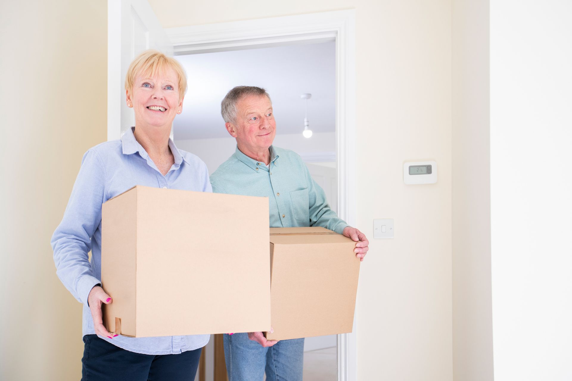 Couple carrying cardboard boxes through a doorway, smiling.