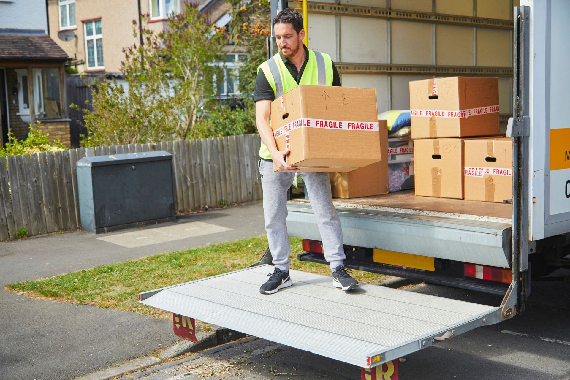 Delivery person in vest loading boxes from truck ramp.
