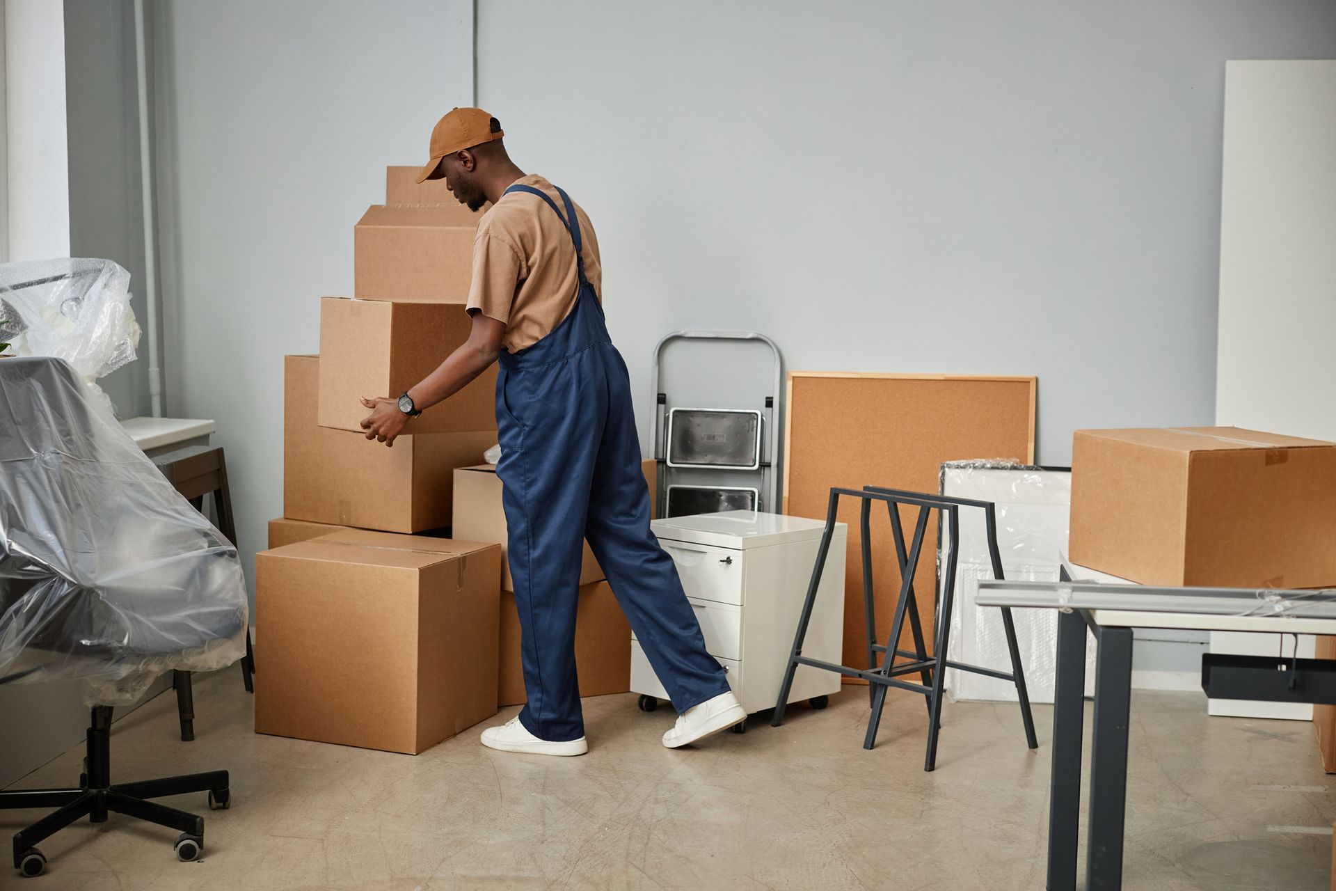 Person in blue overalls stacking cardboard boxes in an office; moving items.