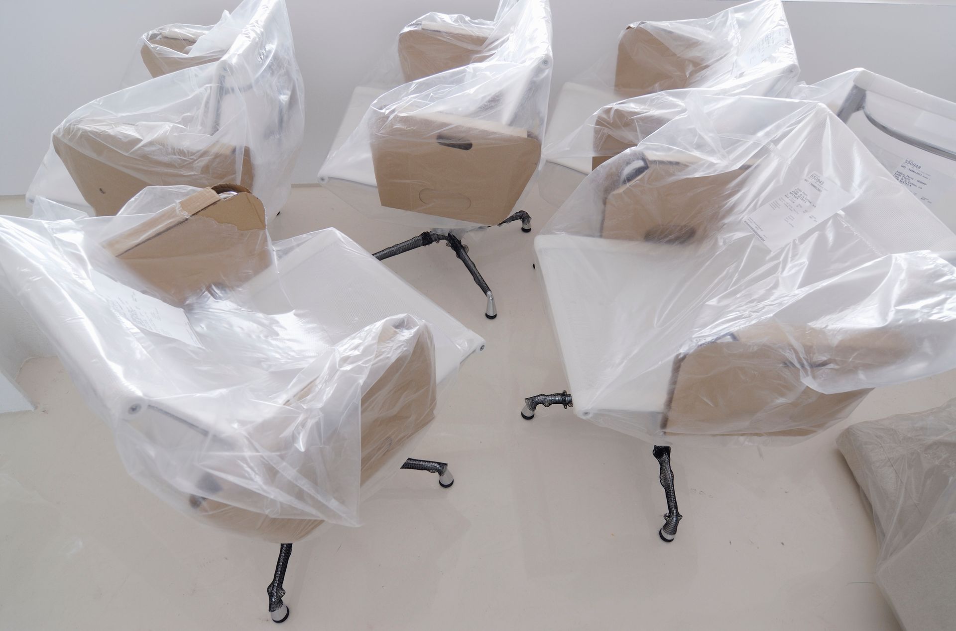 Chairs wrapped in plastic and cardboard, presumably new and ready for use, arranged in a white room.
