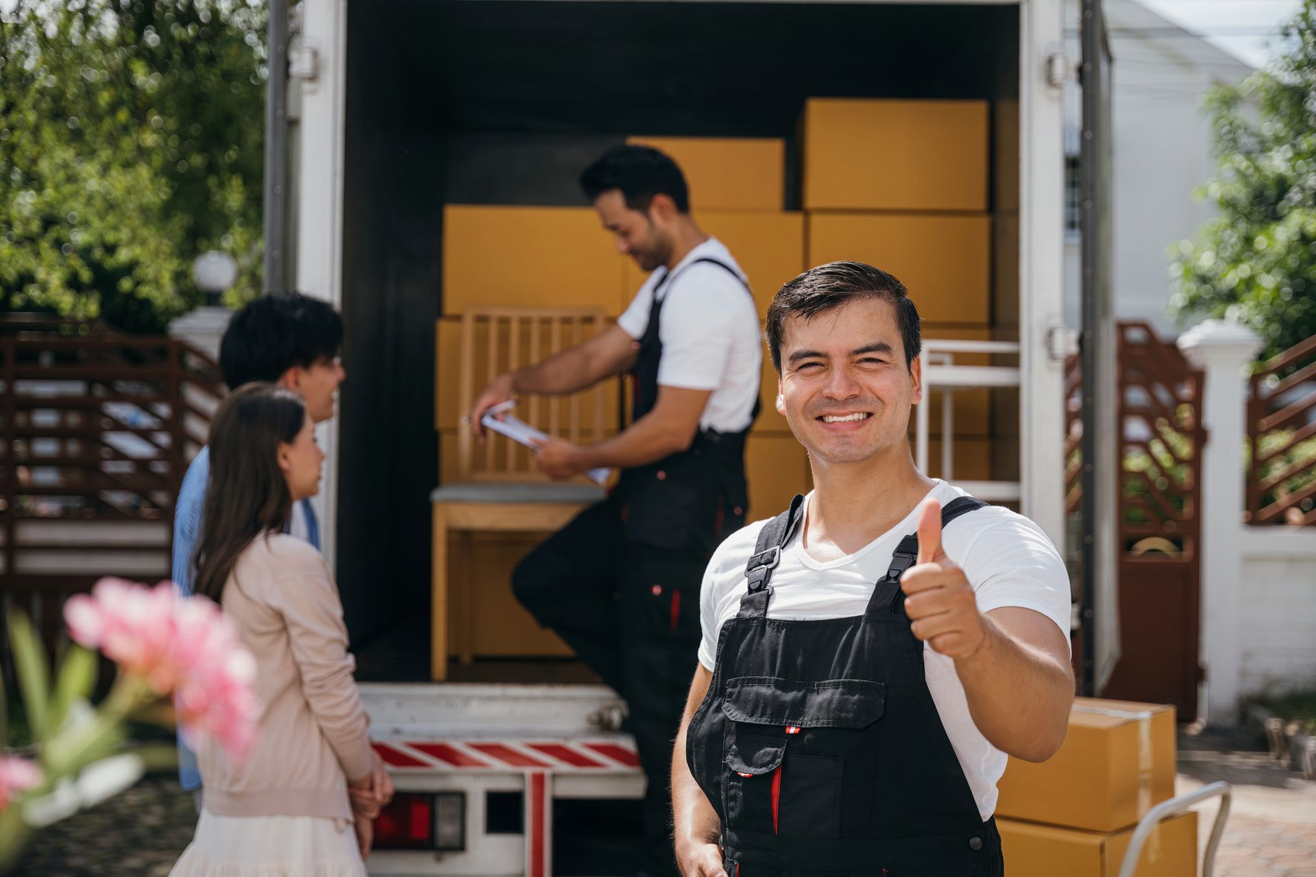 Movers loading boxes into truck; man smiles and gives thumbs up. Family observes.