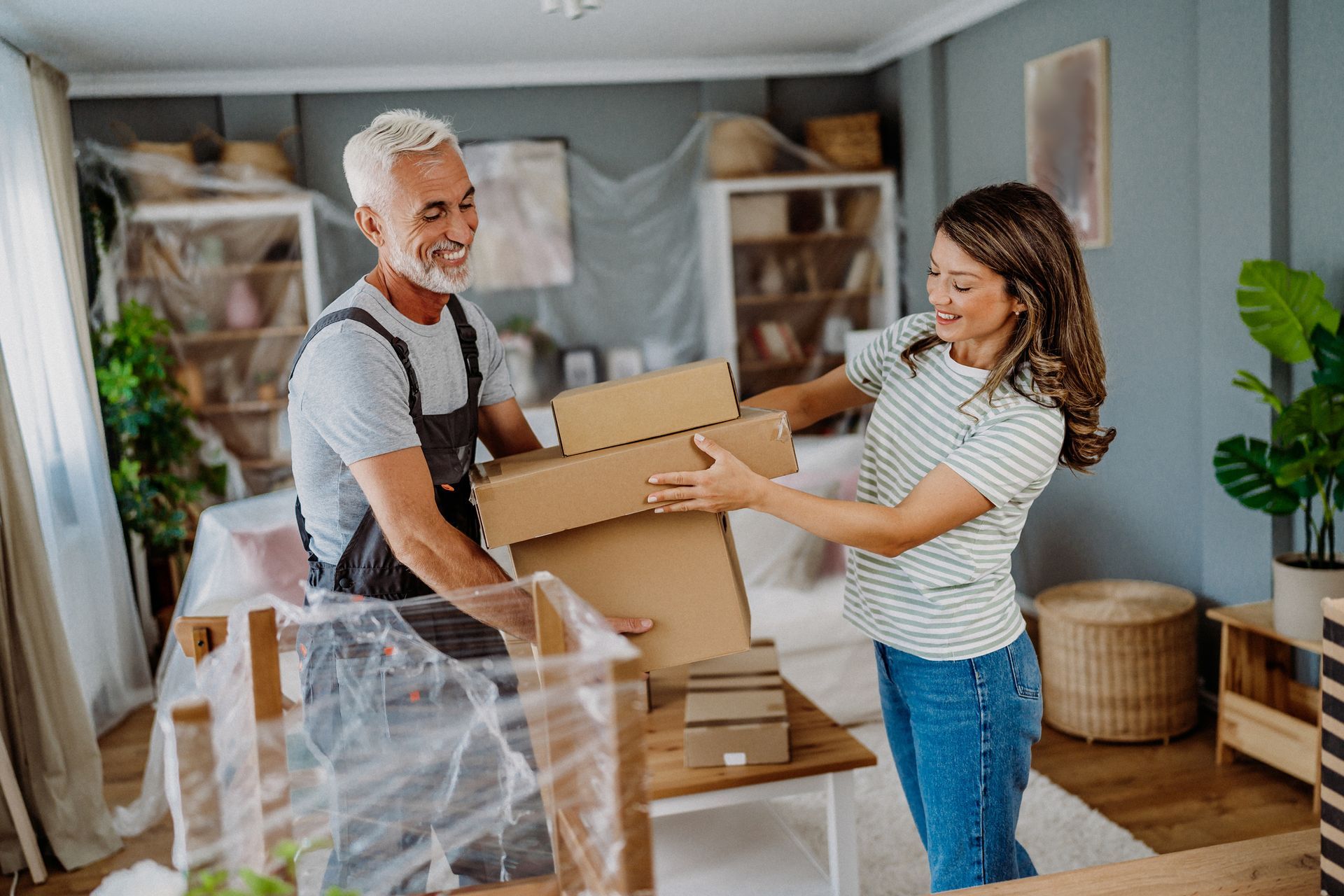 Man passing cardboard boxes to woman in a room, smiling. Moving.