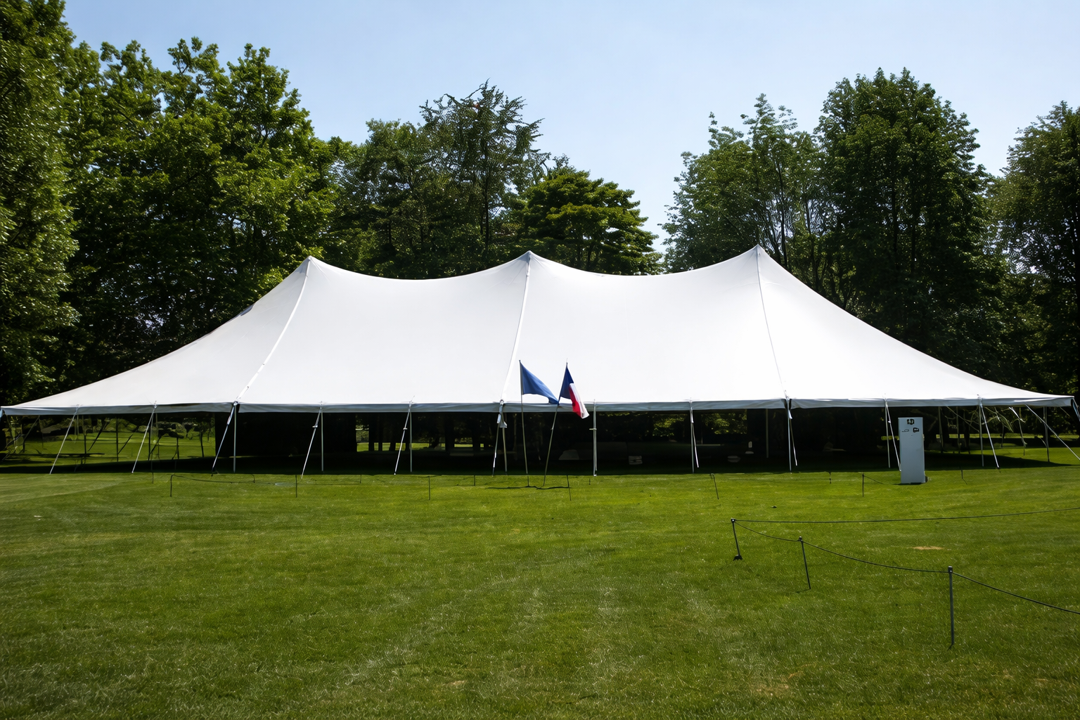 White event tent on a grassy lawn with trees in the background, blue sky.