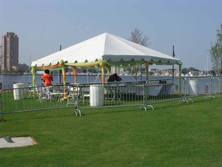 White tent on green grass with metal barricades, a waterfront, and a person.
