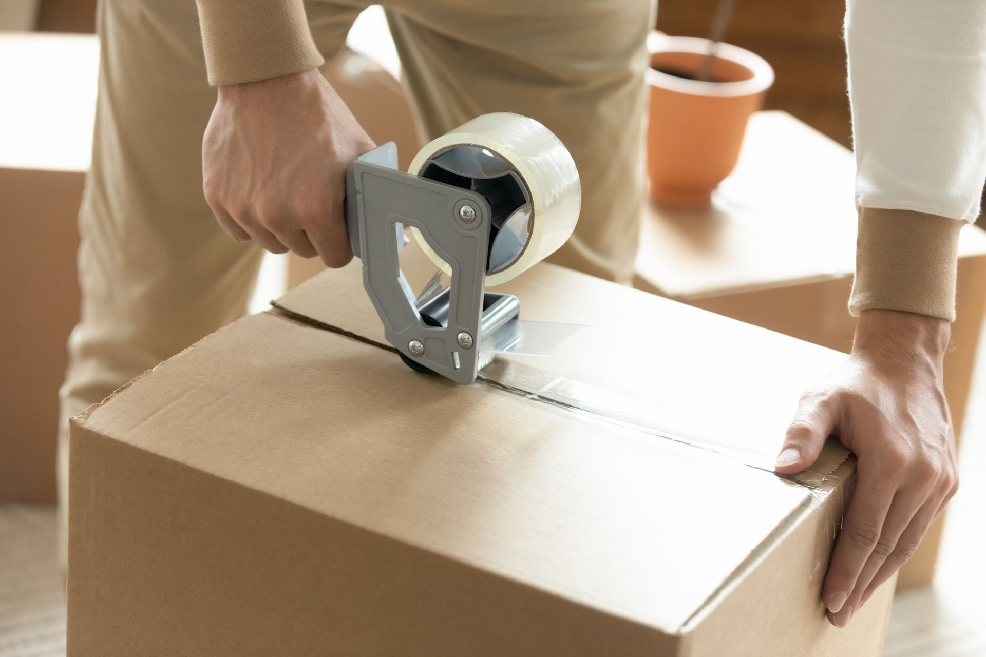 Person seals a cardboard box with packing tape, preparing for a move.