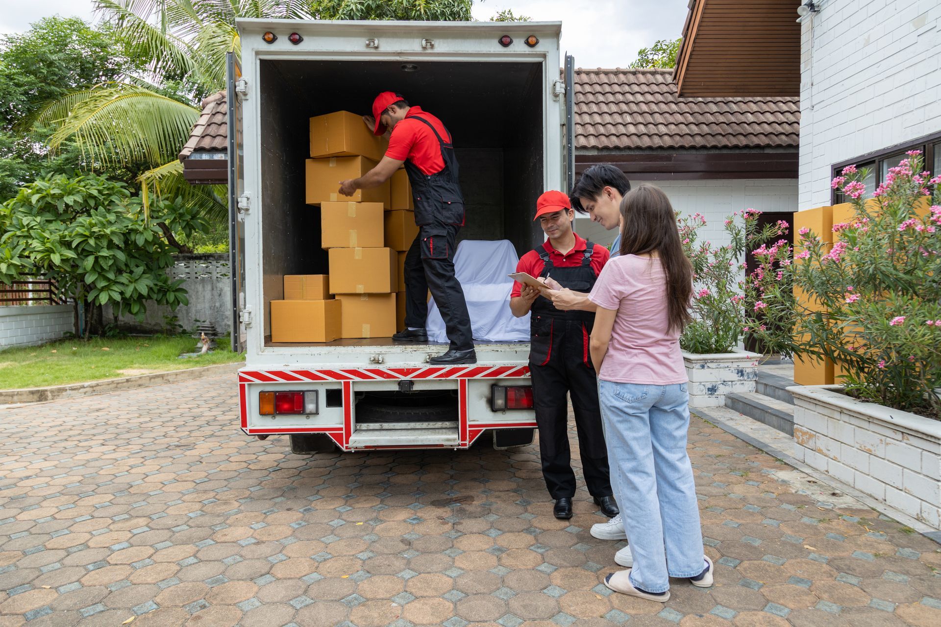 Movers loading boxes into truck. Two people watch. House in background.