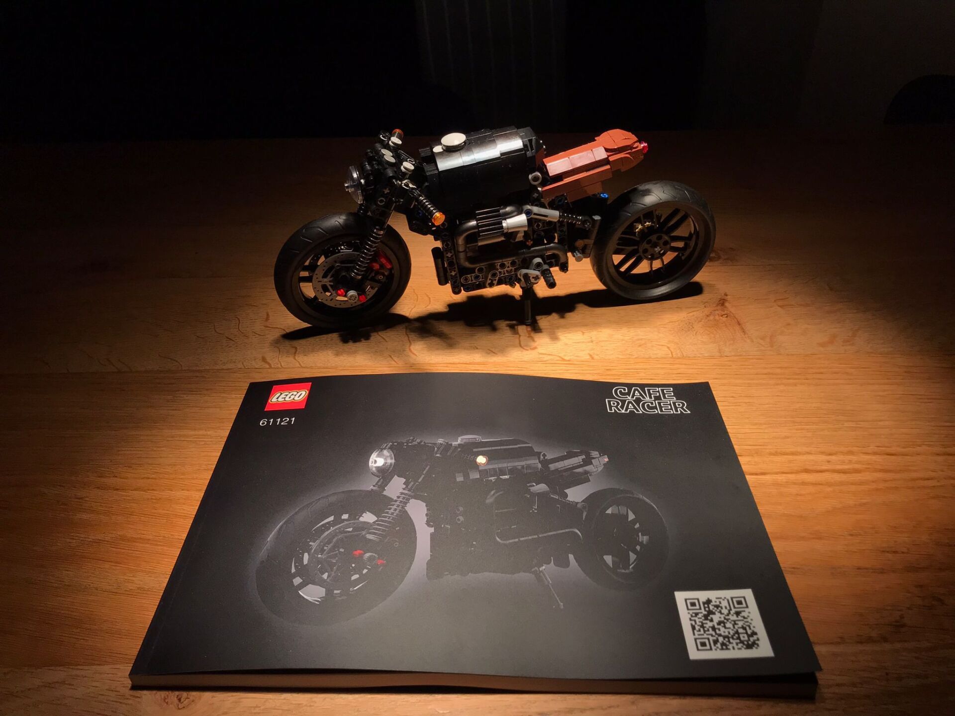 A black motorcycle is sitting on top of a black book on a wooden table.