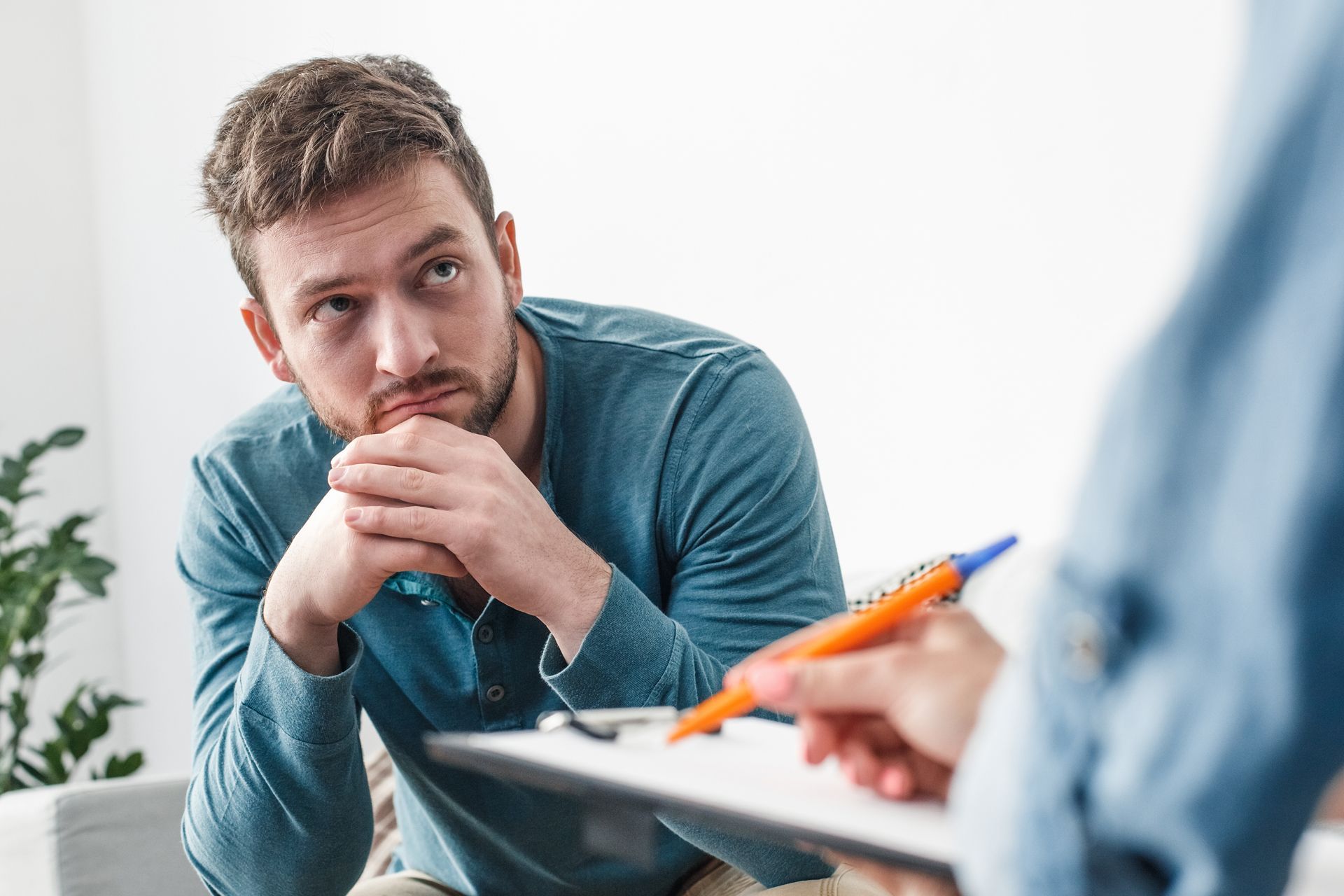 A man is sitting on a couch talking to a psychologist holding a clipboard
