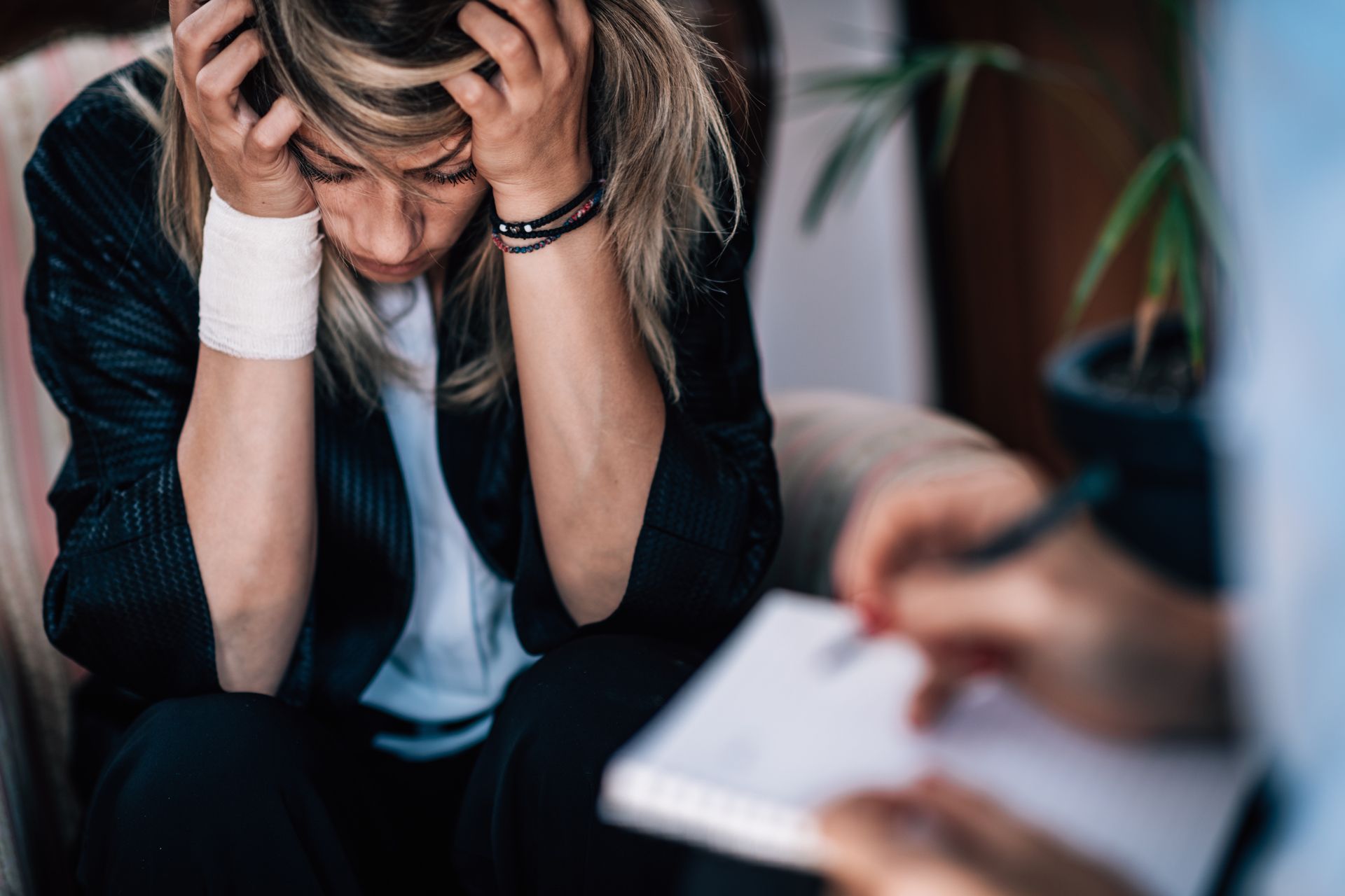 A woman is sitting in a chair with her head in her hands while a person writes in a notebook