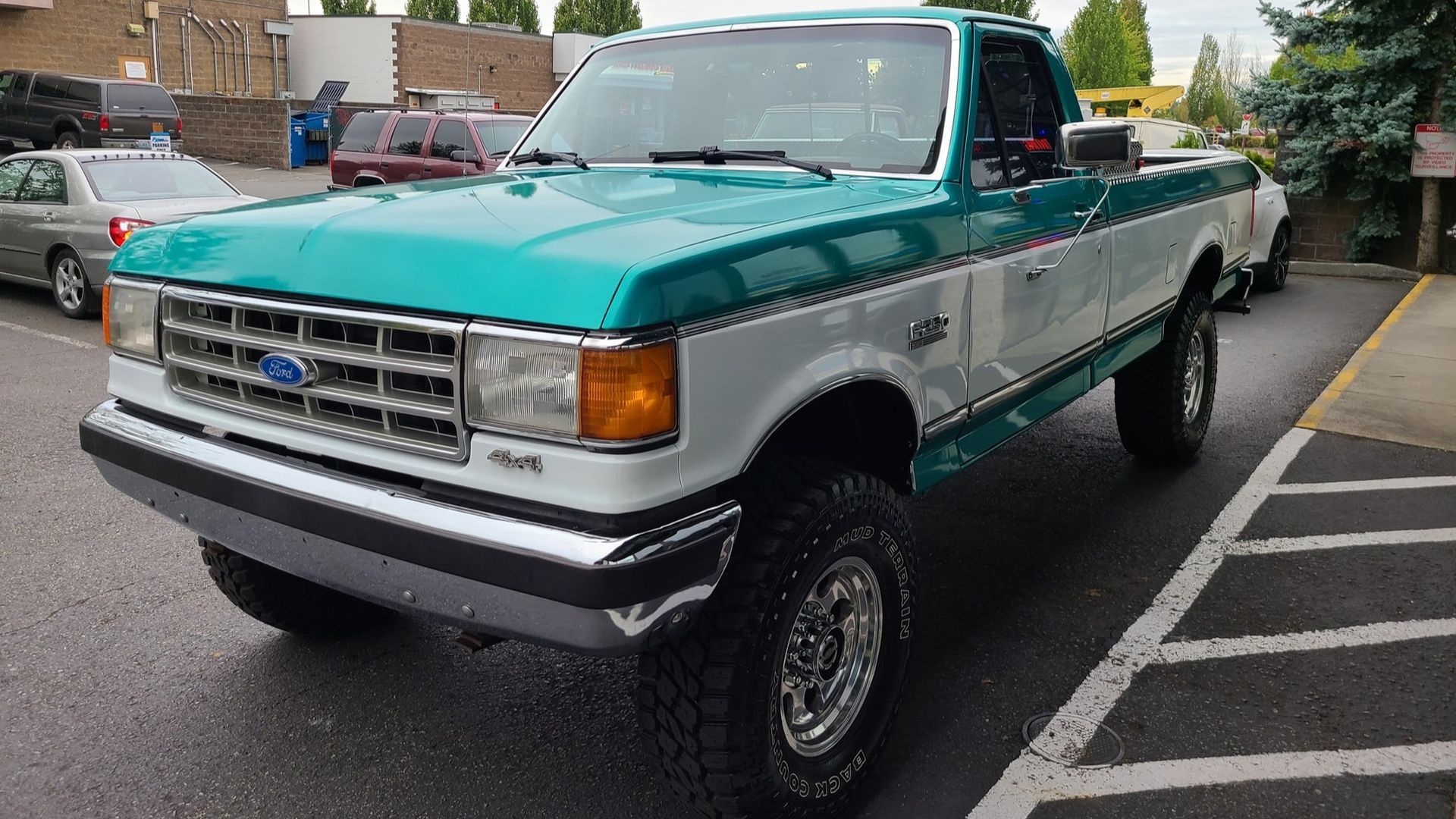 A green and white ford truck is parked in a parking lot.