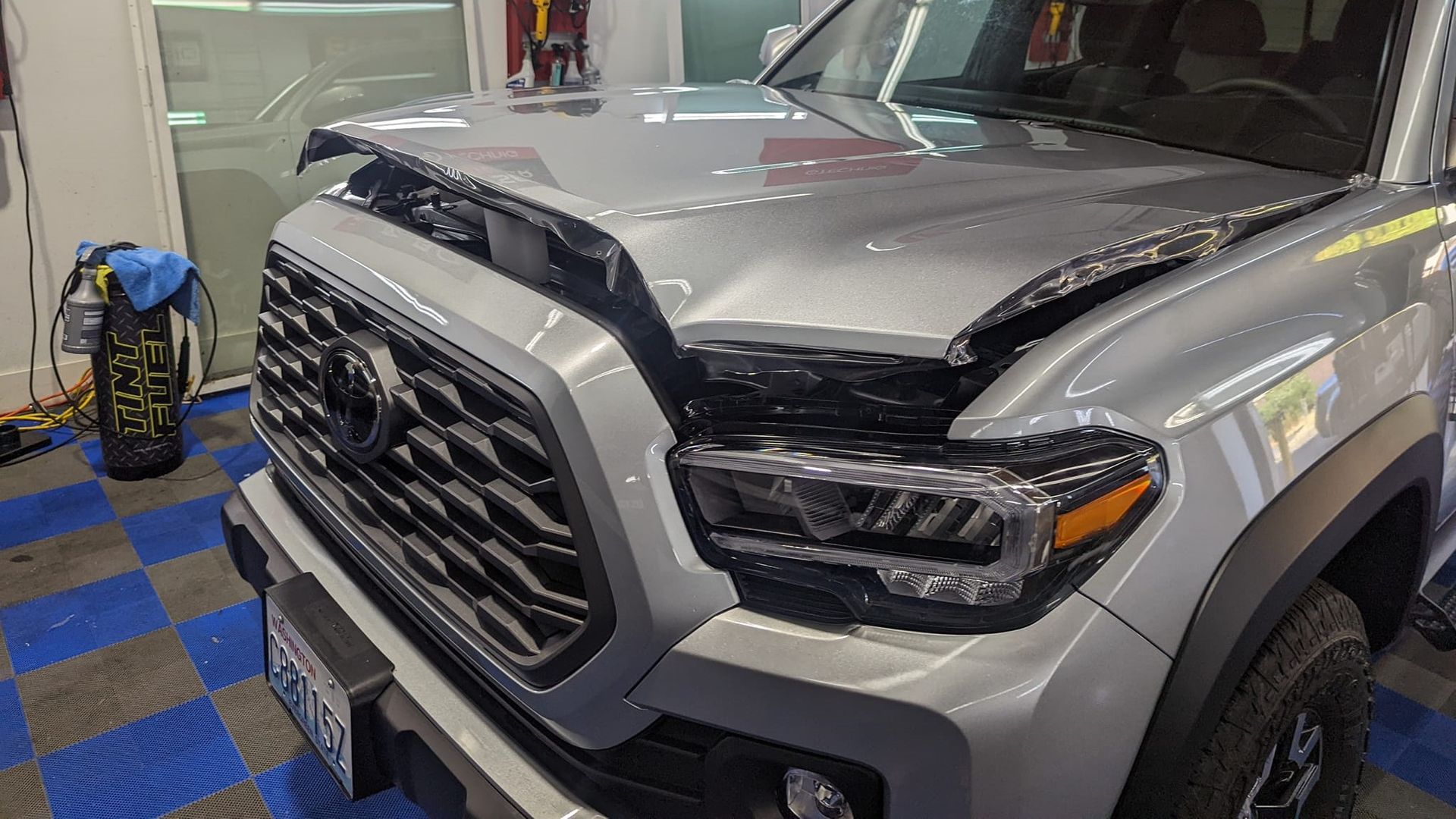 A silver toyota tacoma is parked in a garage with its hood up.