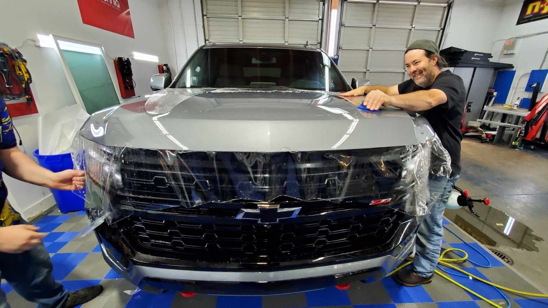 Two men are wrapping a car with plastic wrap in a garage.