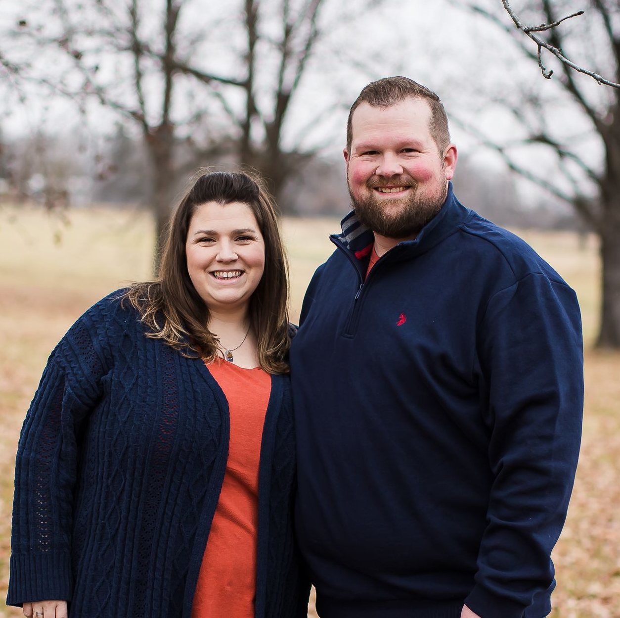 Man and wife standing together with a blurred outdoor background.