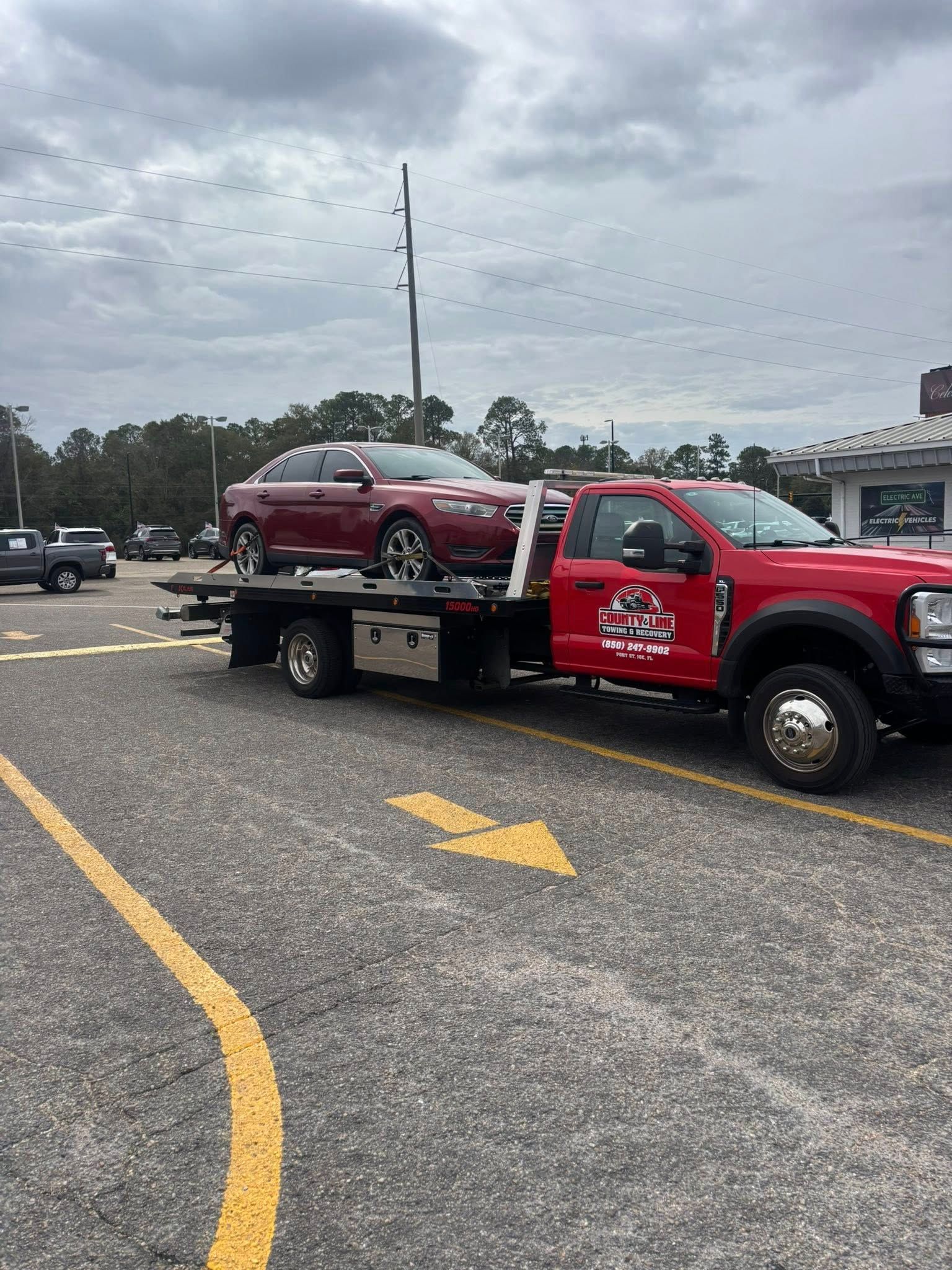 Red car on a tow truck in a parking lot on a cloudy day. The truck is also red.