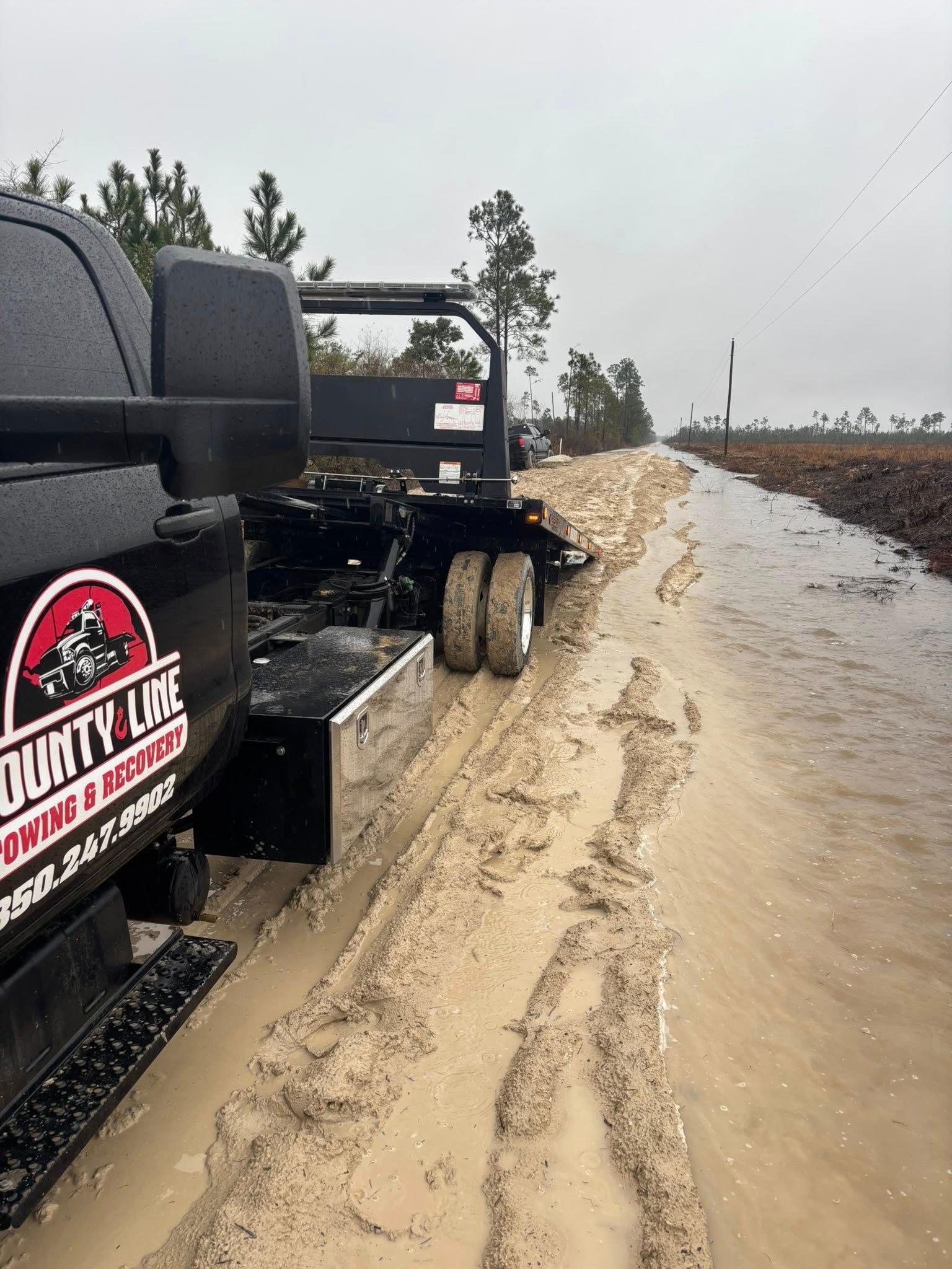 Black truck and trailer stuck in muddy, flooded road. The words