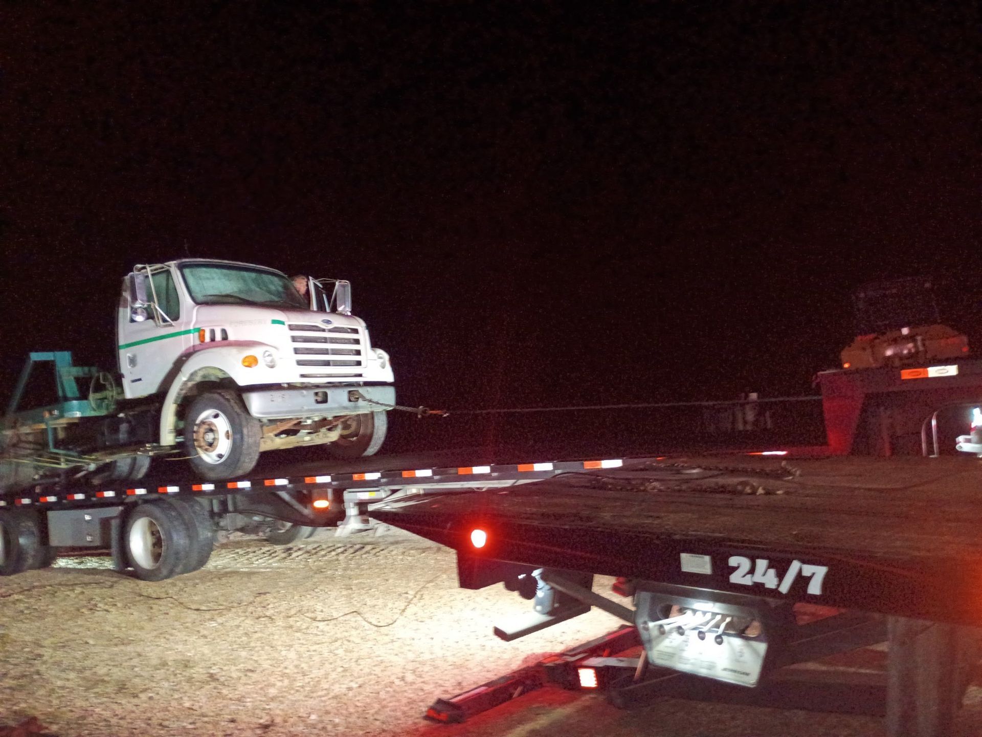 Tow truck loading a white truck onto its flatbed at night.