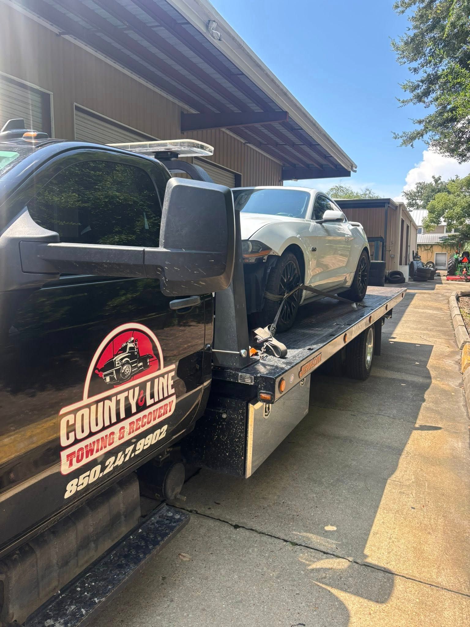 A white car with front-end damage loaded on a flatbed tow truck with 