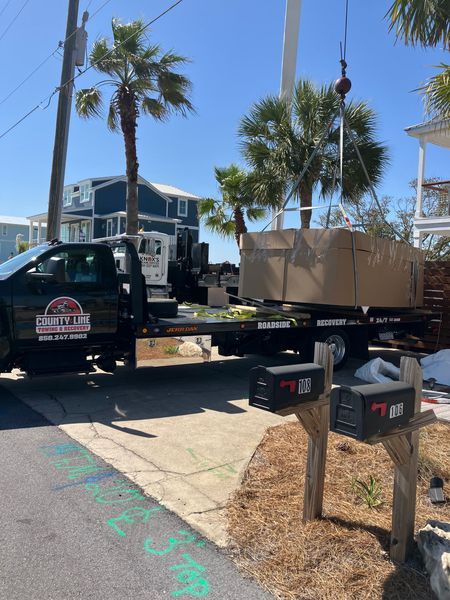 A flatbed truck with a large, wrapped object is parked near mailboxes, under a crane.