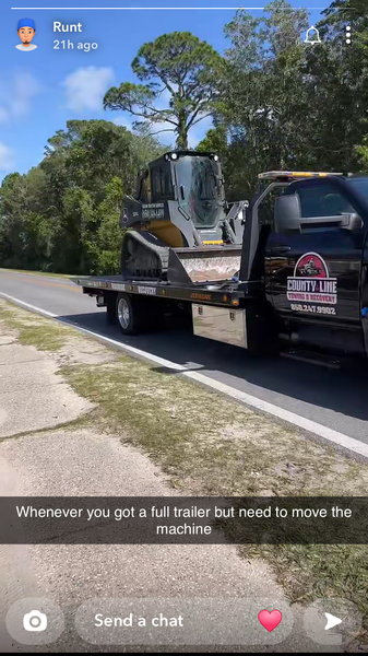Skid steer on a flatbed tow truck traveling on a road.