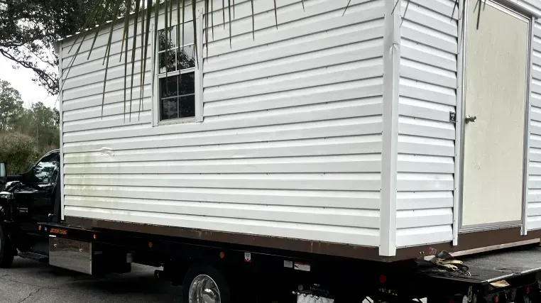 White shed with window and door on a flatbed truck.