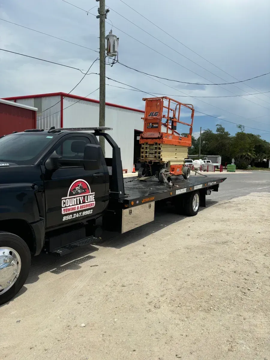 Black tow truck transporting an orange aerial lift, parked on a paved road.