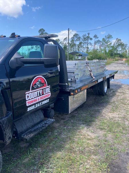 Black County Line Towing truck with a flatbed carrying metal sheets, parked outside.