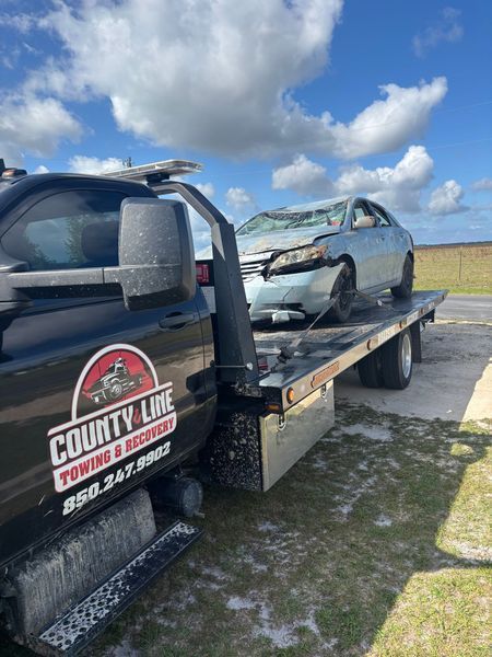 A damaged light blue car on a flatbed tow truck. 