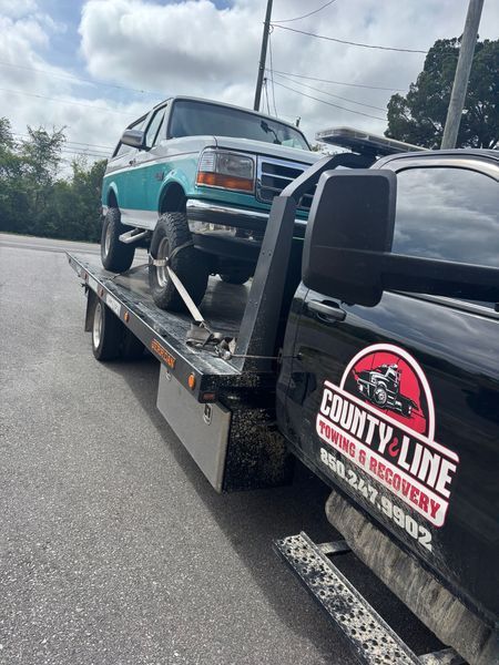 Ford Bronco being towed on a flatbed tow truck. The truck is black with 