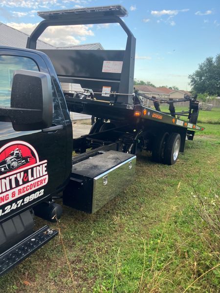 Black tow truck with a flatbed in a grassy area, 
