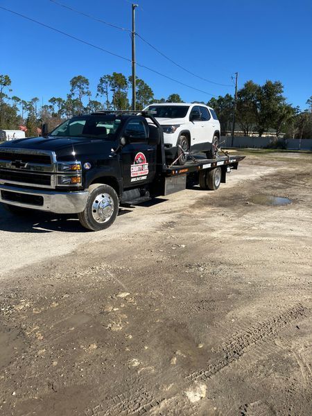 Black tow truck carrying a white SUV on a sunny day.