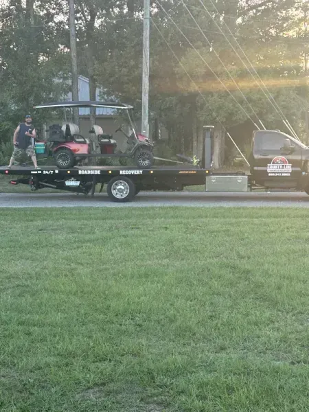 A golf cart loaded onto a flatbed tow truck with a person standing by.