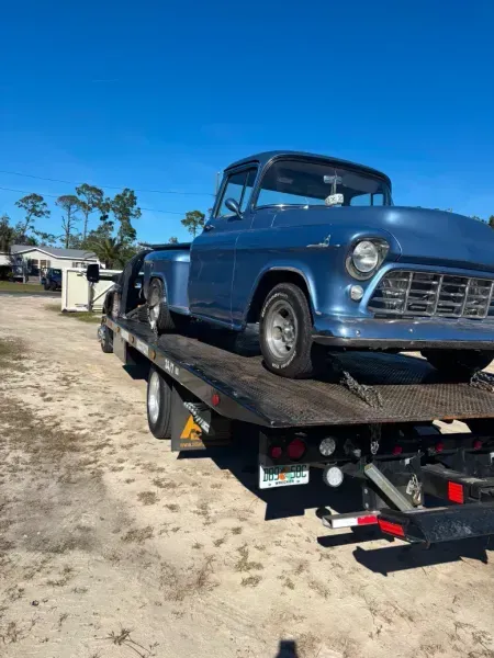 Blue vintage pickup truck on a flatbed tow truck on a sunny day.