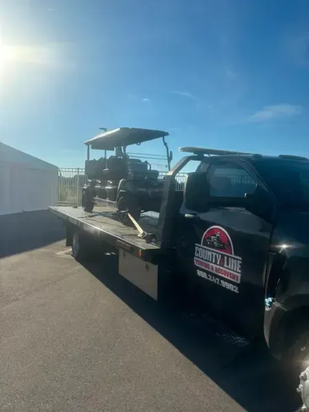 Black tow truck with tractor on flatbed in sunny setting.
