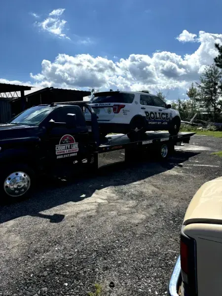 A tow truck carrying a police SUV on a sunny day.