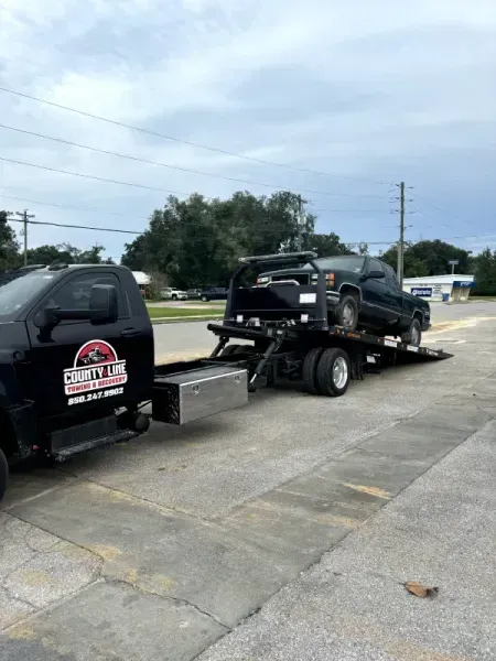 Black tow truck hauling a black pickup truck on a sunny day.
