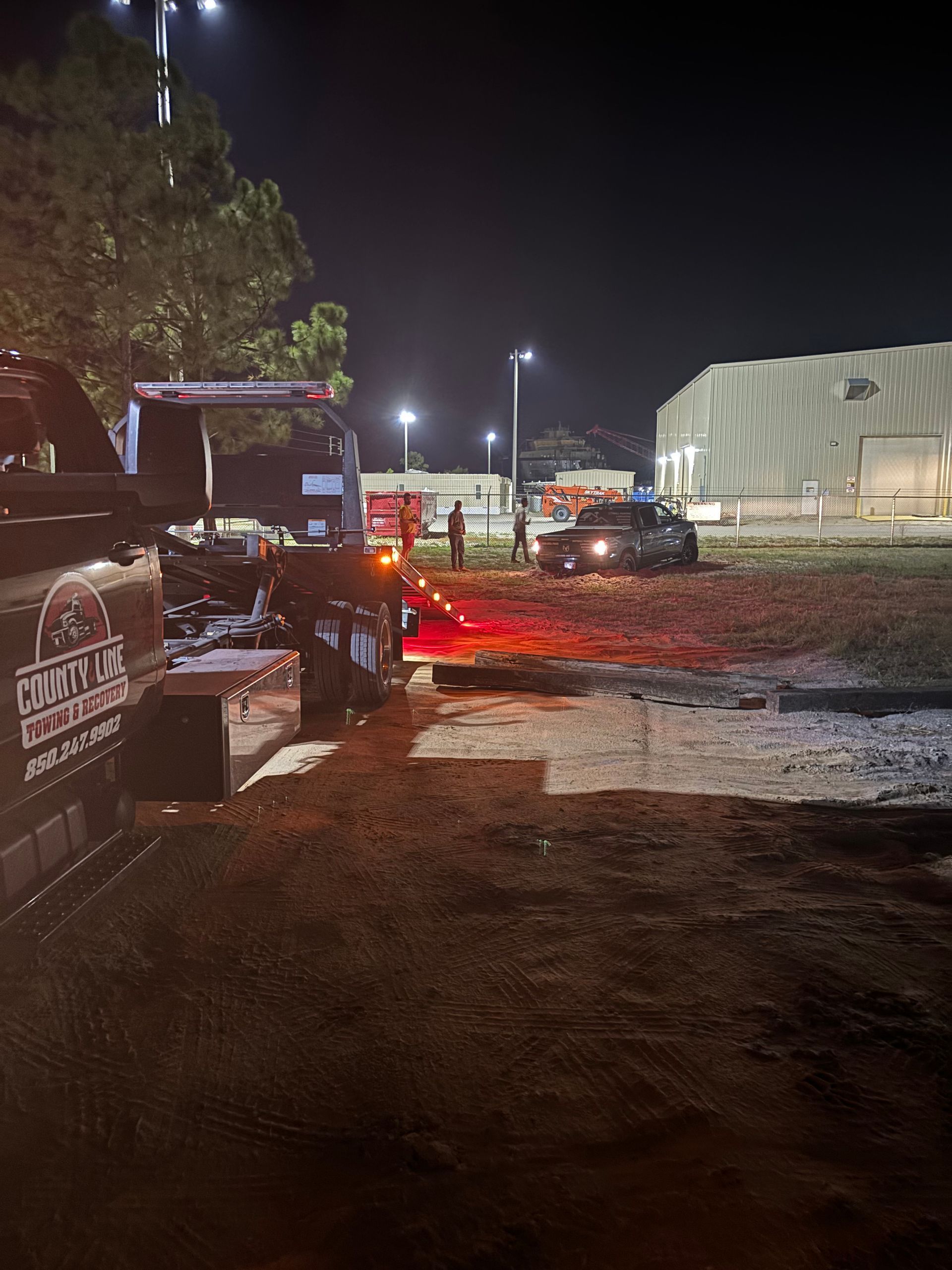Tow truck pulling a car at night near a building and light posts.