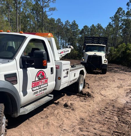 A silver pickup truck being towed by a County Line Towing truck on a paved road.