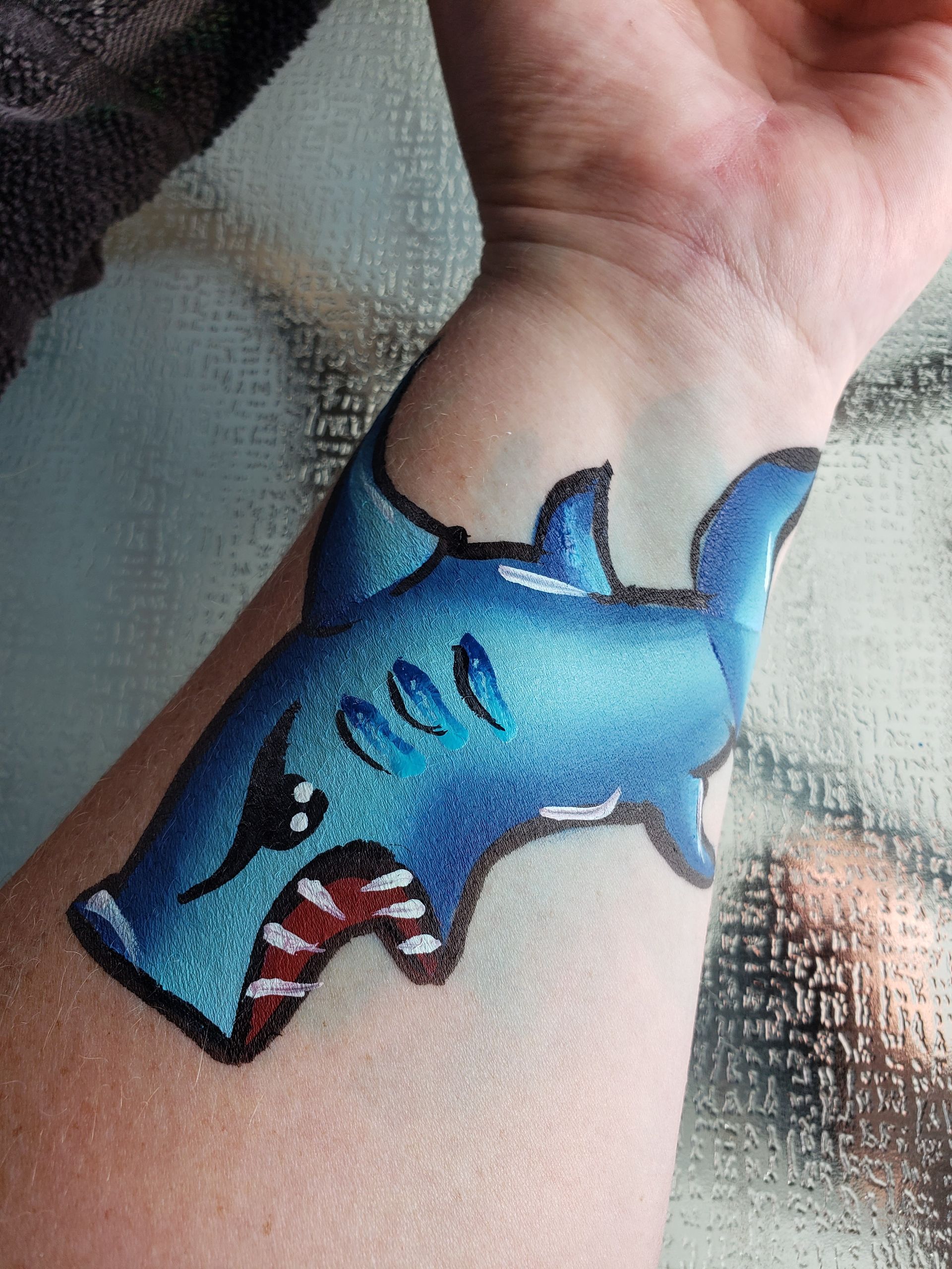 Hand painted blue shark on inner forearm.