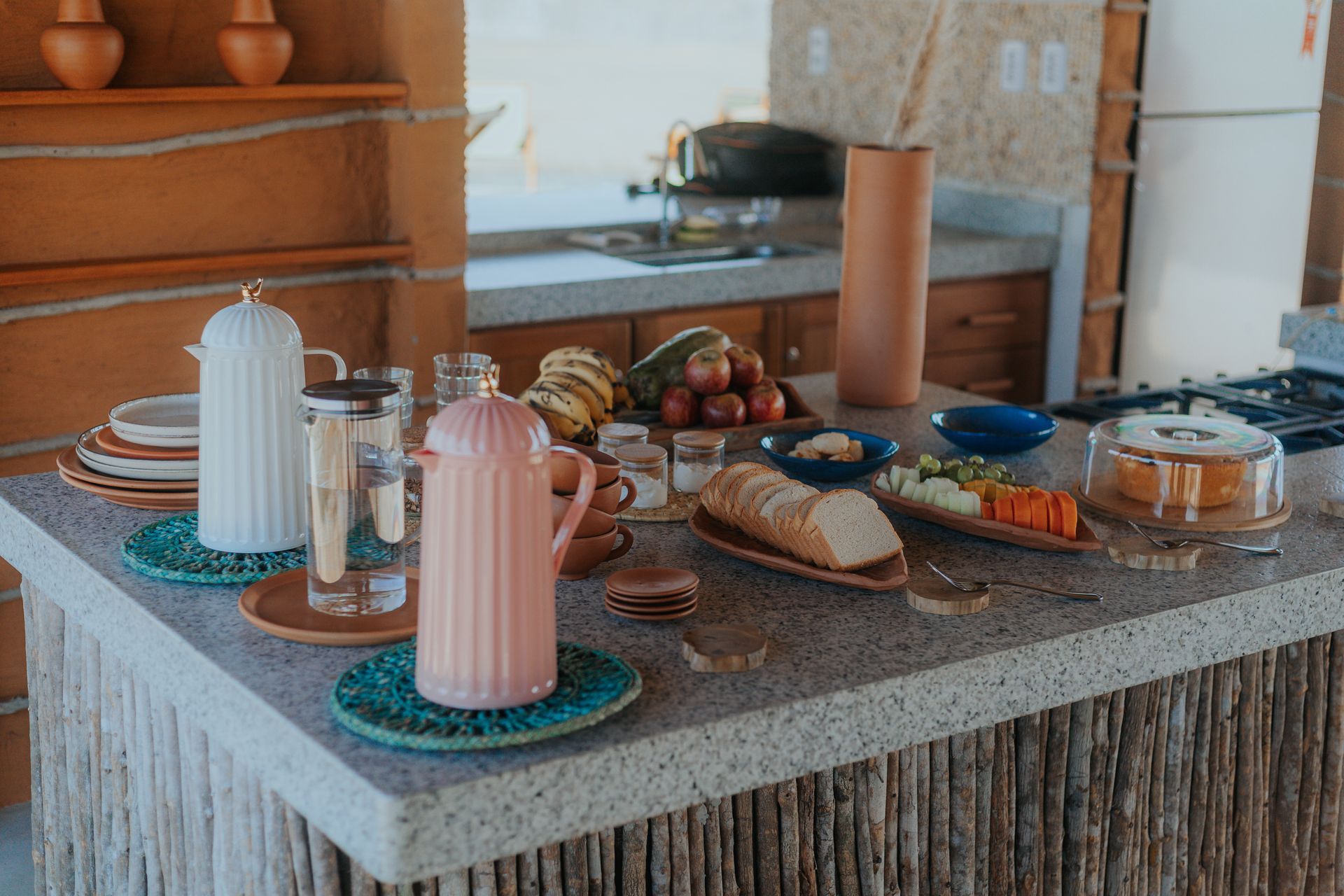 Bancada com opções de café da manhã: pão, frutas, queijo, café e bolo.