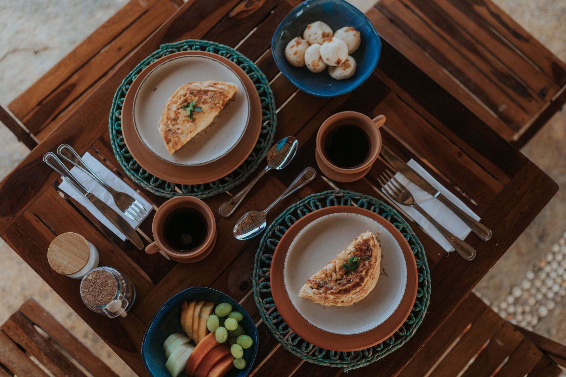 Mesa de café da manhã posta para dois com pratos de comida, café e frutas.
