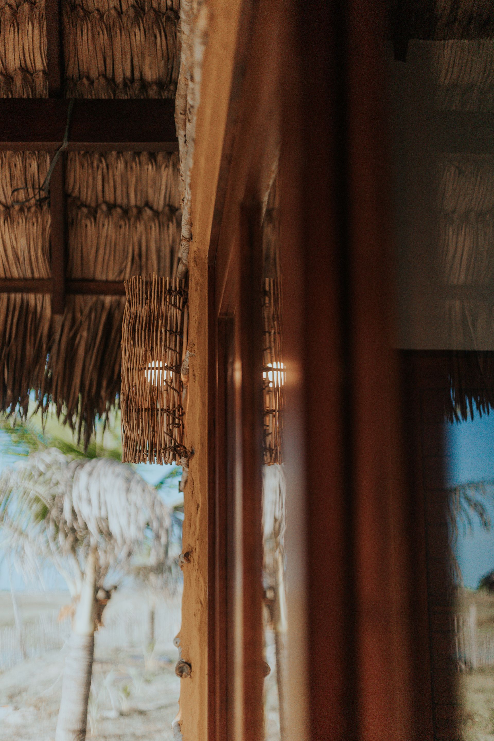 Caixilho de janela de madeira com vista para uma paisagem tropical com telhado de palha.