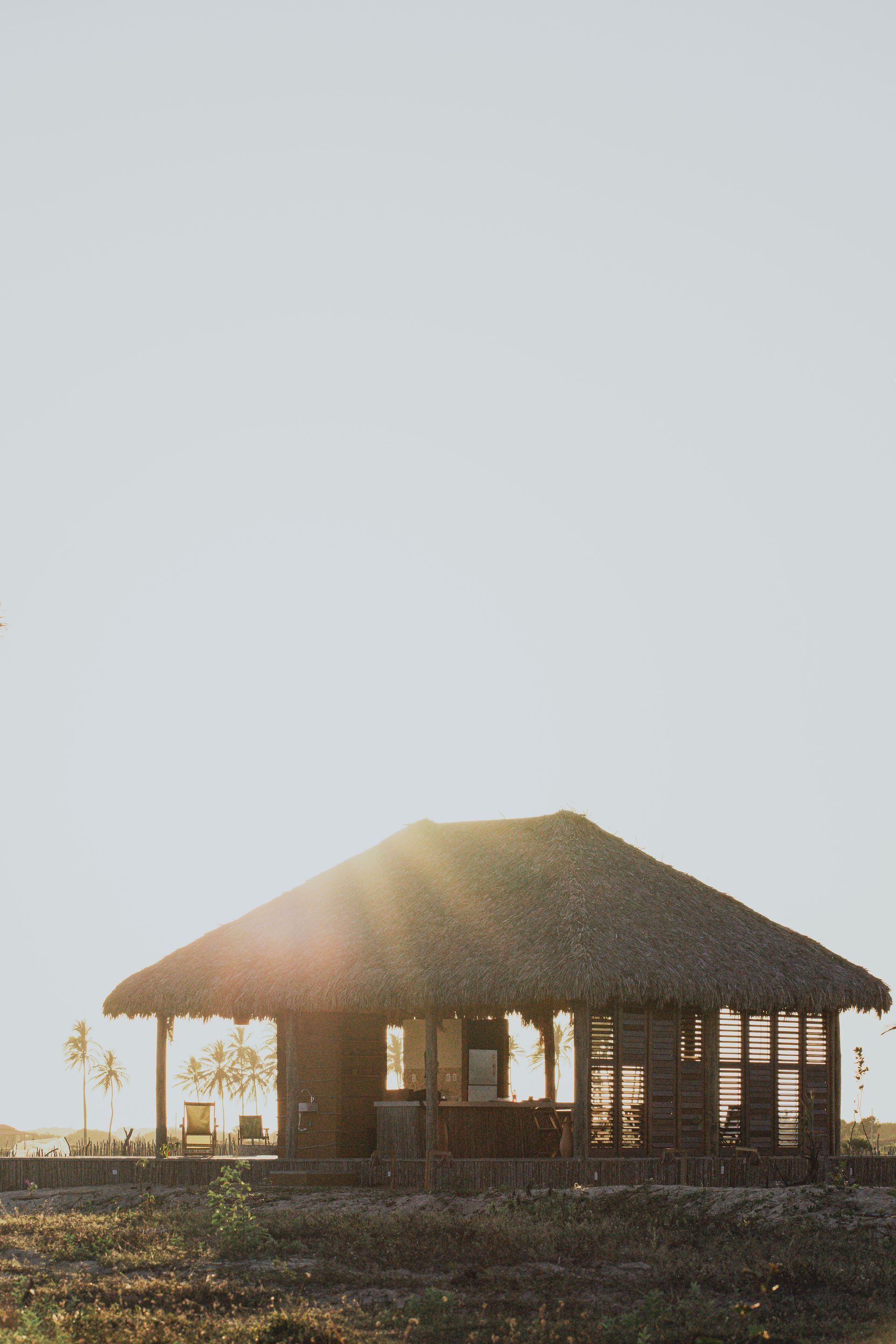 Cabana com teto de palha e laterais abertas, banhada por luz solar intensa.