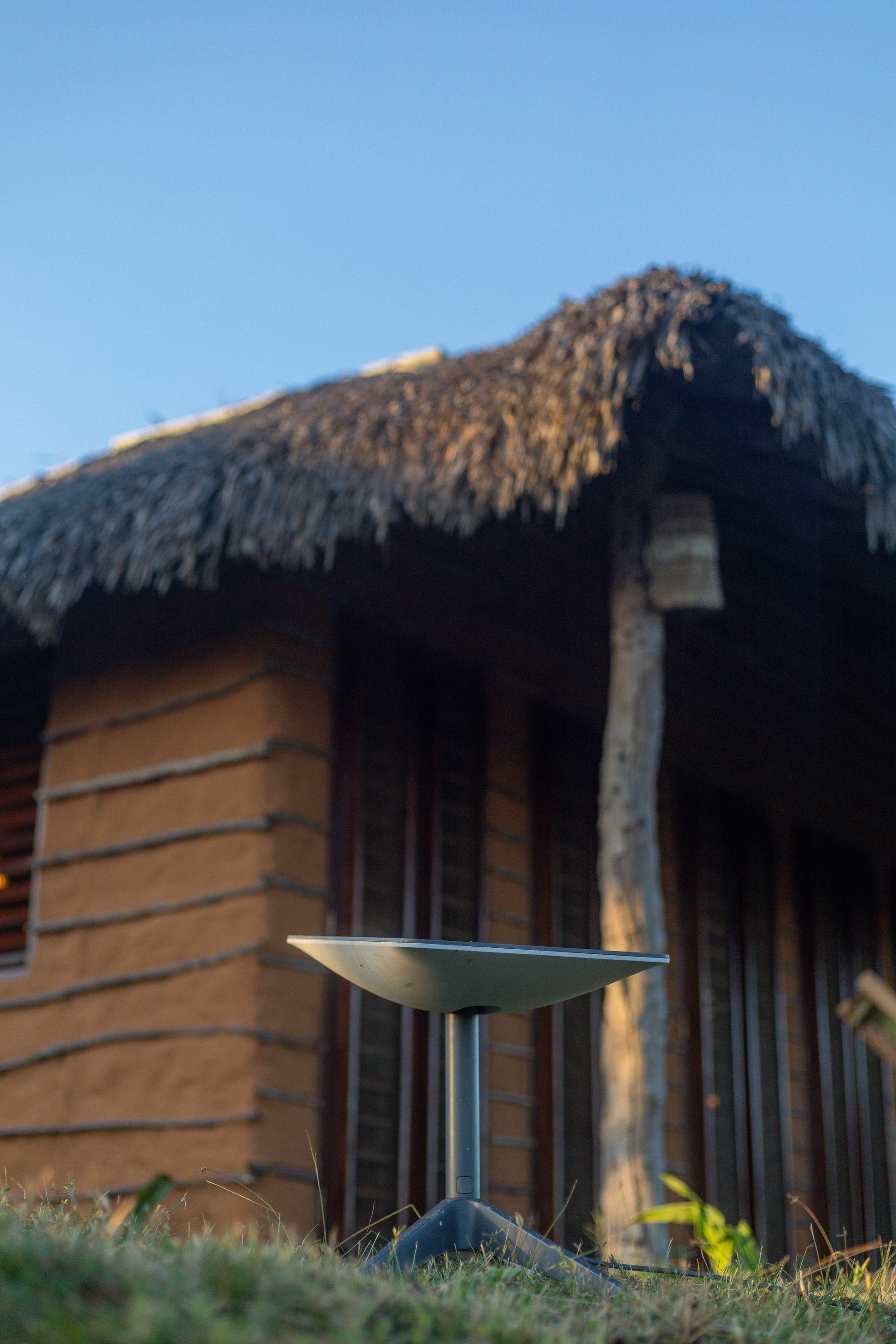 Uma mesa de metal está em frente a uma construção rústica de madeira com telhado de palha.