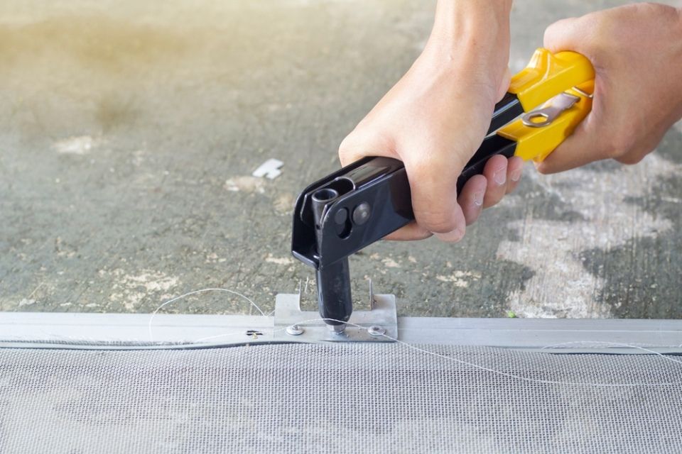 A person is using a pair of pliers to fix a screen door.