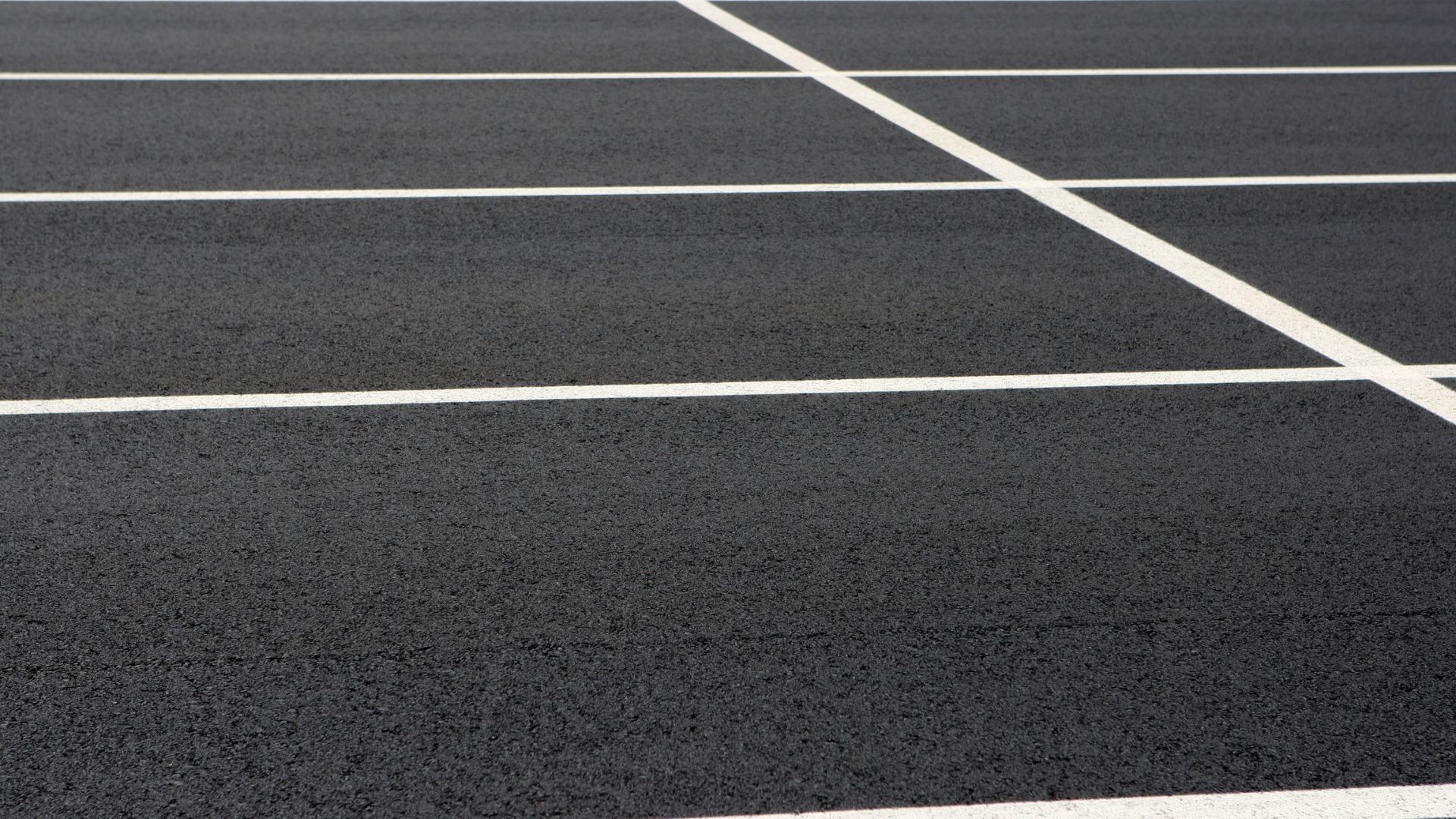 A top-down view of freshly paved asphalt with white painted parking space lines.