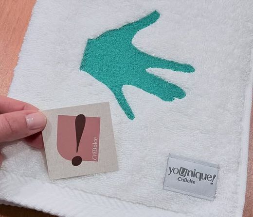 Una mano che tiene un asciugamano bianco con un'impronta di mano turchese e due piccole etichette.